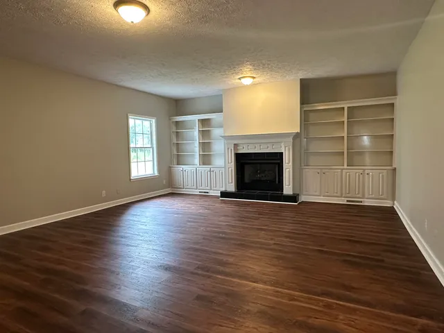 an empty room with wooden floor fireplace and windows