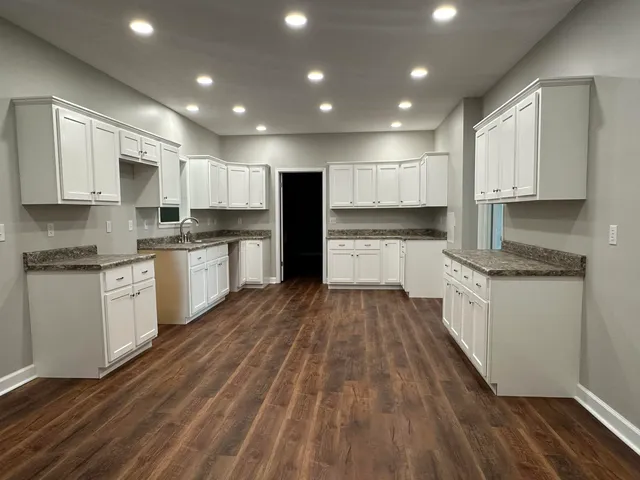 a large kitchen with kitchen island granite countertop a stove top oven a sink a counter space and cabinets