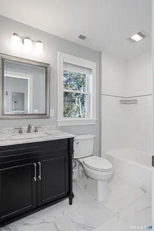a bathroom with a granite countertop toilet a sink a mirror and a window