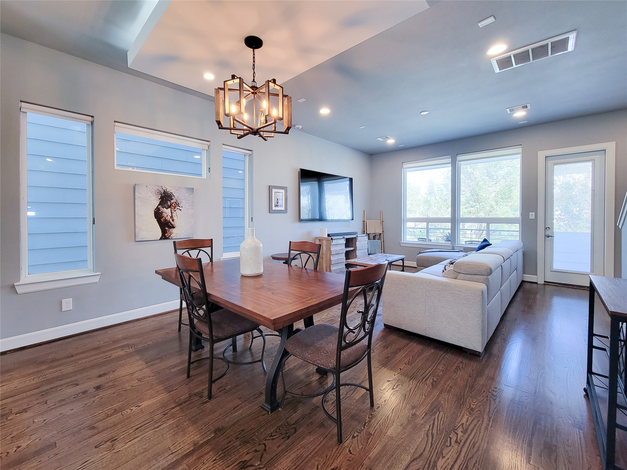 1705 Eado Point Lane Houston, TX 77003 - Photo 24 of 50 An open-concept living and dining area with hardwood floors, ample natural light from large windows, and stylish lighting fixtures. The space features a cozy seating arrangement with a sectional sofa, a wall-mounted TV, and a contemporary dining table, making it ideal for both entertaining and relaxation.