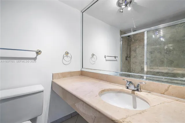 a bathroom with a granite countertop sink a toilet a mirror and shower