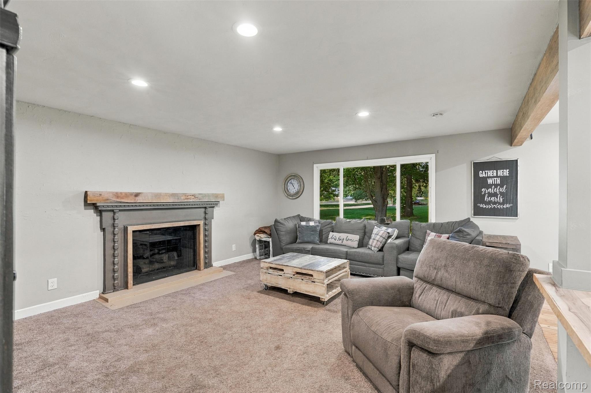 Recessed ceiling lighting, carpeted flooring, large window, decorative fireplace with mantel, and exposed ceiling beam