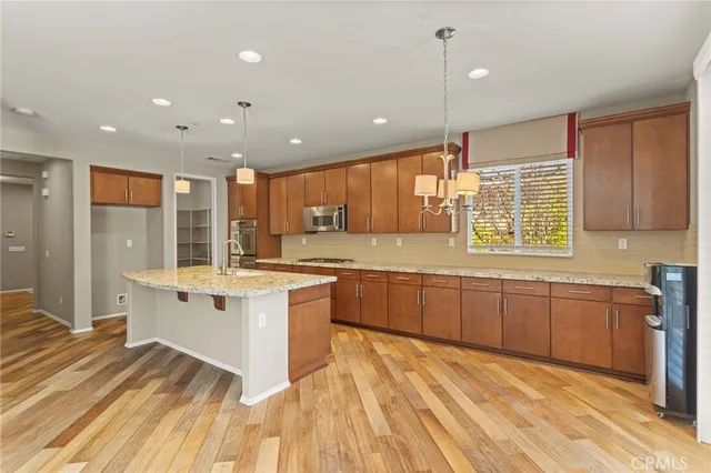 a large kitchen with stainless steel appliances granite countertop a large kitchen island a stove a sink dishwasher a refrigerator and wooden cabinets with wooden floor