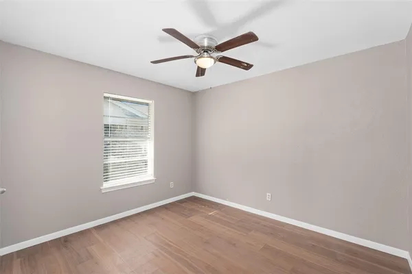 an empty room with wooden floor ceiling fan and windows