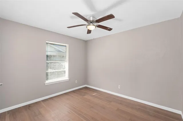 an empty room with wooden floor ceiling fan and windows