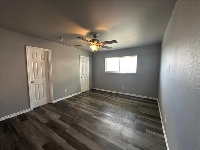 a view of an empty room with wooden floor and a chandelier fan