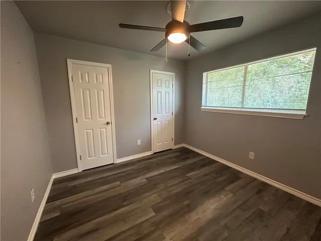 an empty room with wooden floor fan and windows
