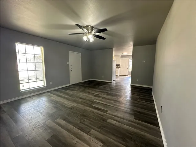 an empty room with wooden floor chandelier fan and windows