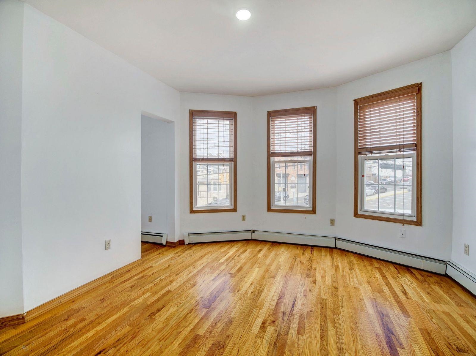 921 Paterson Plank Road, Unit 2 North Bergen, NJ 07047 - Photo 5 of 15 an empty room with wooden floor and windows