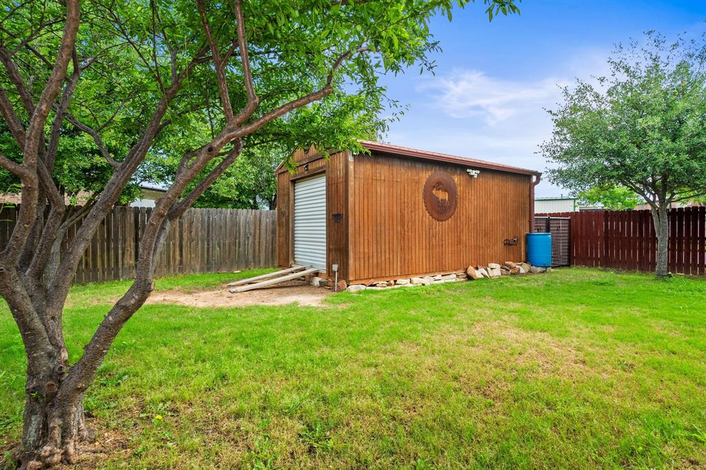 1401 Hickory Drive Pilot Point, TX 76258 - Photo 22 of 34 Freestanding shed with corrugated metal siding, a roll-up door, and an attached gutter system