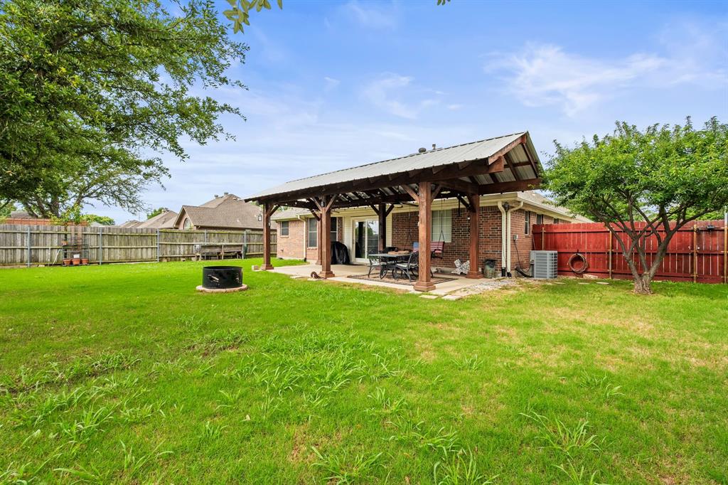 1401 Hickory Drive Pilot Point, TX 76258 - Photo 23 of 34 Expansive backyard featuring a covered patio with a metal roof, a brick exterior, a wood privacy fence, and a fire pit