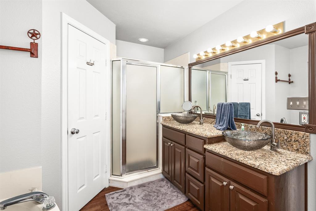 1401 Hickory Drive Pilot Point, TX 76258 - Photo 9 of 34 Dual vanity with vessel sinks and granite countertops, dark wood cabinetry, a glass-enclosed corner shower, and wood-finish flooring