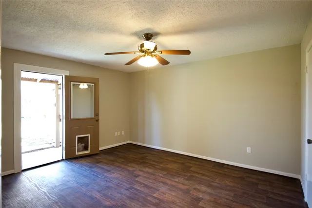 an empty room with wooden floor chandelier fan and windows