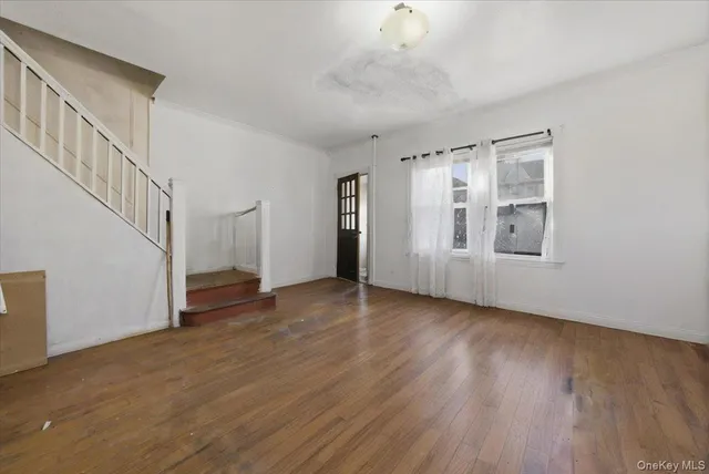 a view of an empty room with wooden floor and stairs