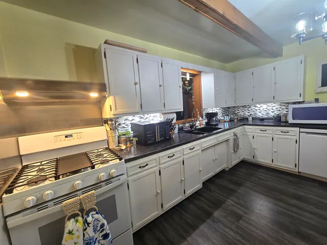 a large white kitchen with stainless steel appliances granite countertop a stove and a sink