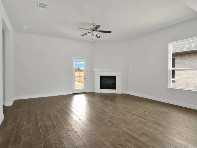 an empty room with wooden floor chandelier fan and windows