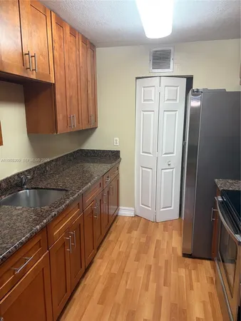 a kitchen with stainless steel appliances granite countertop a refrigerator a sink dishwasher and wooden cabinets with wooden floor