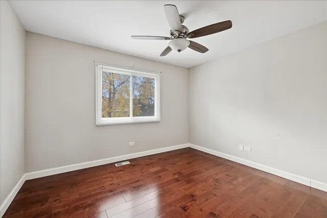 an empty room with wooden floor fan and windows