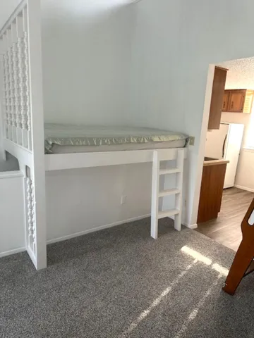 a view of an empty room with wooden floor and a kitchen