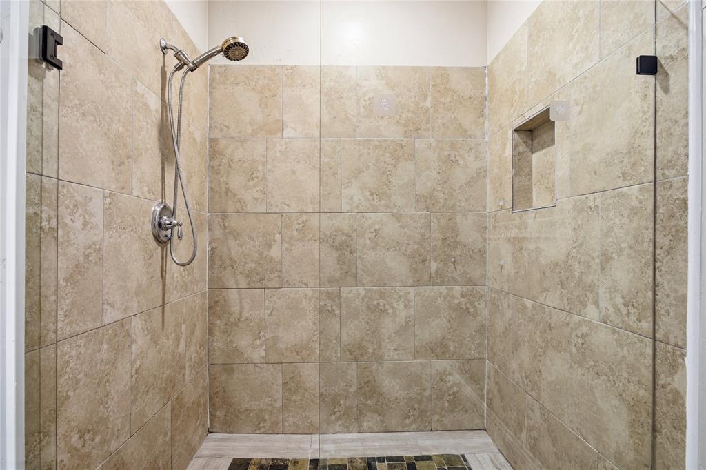 1502 Reed Street Greenville, TX 75401 - Photo 17 of 26 Tiled shower enclosure featuring light-toned large format ceramic tiles, a built-in shower niche, and a chrome shower fixture with a handheld sprayer