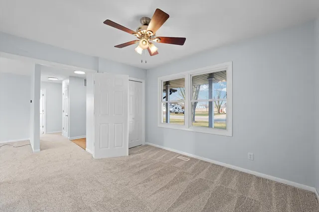 an empty room with chandelier fan and windows