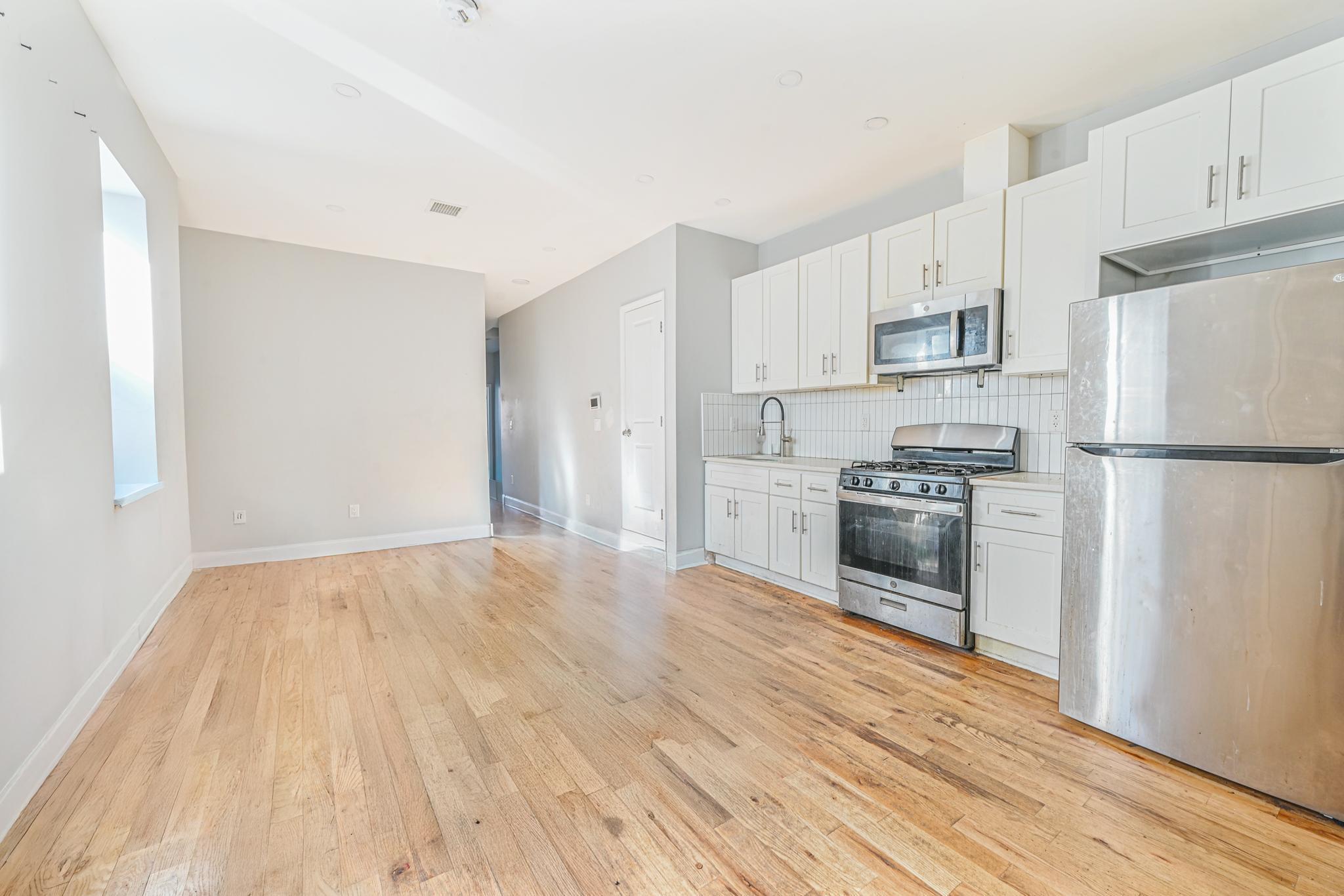 2243 Bathgate Avenue Bronx, NY 10457 - Photo 13 of 26 Kitchen featuring sink, white cabinetry, stainless steel appliances, decorative backsplash, and light wood-type flooring