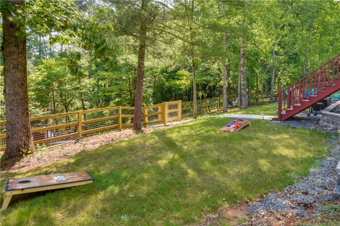 206 Petty Road Seneca, SC 29672 - Photo 40 of 48 A sloped grassy yard with a wooden fence and mature trees creates a serene outdoor space.
