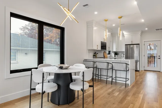 a kitchen with stainless steel appliances kitchen island granite countertop a stove a refrigerator a dining table and chairs with wooden floor