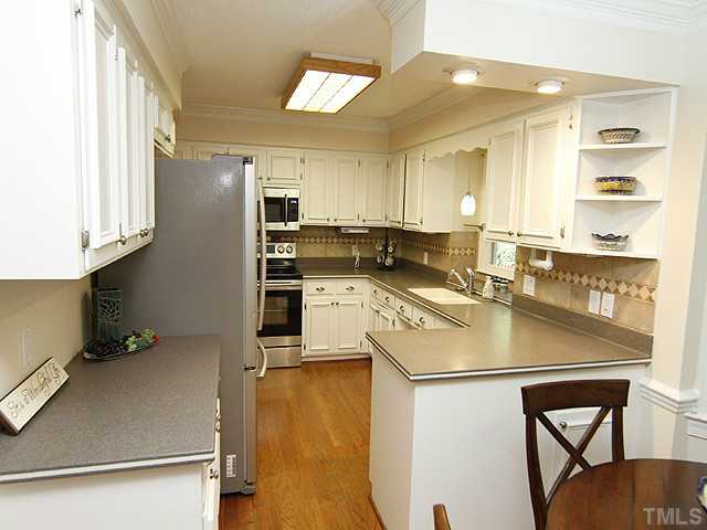 7908 Farnham Court Raleigh, NC 27615 - Photo 8 of 25 Updated Kitchen with Substantial White Cabinets - Solid Surface Counters - Tile Backsplash - Hardwood Floors - Smooth Top Stainless/Black Stove-Microwave-Dishwasher and Pantry. Kitchen Opens to Breakfast Area.