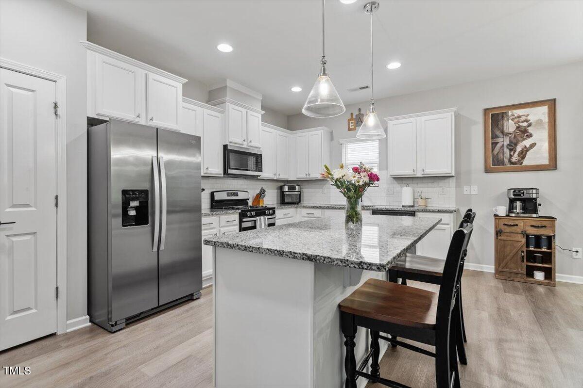 320 Everly Mist Way Wake Forest, NC 27587 - Photo 6 of 34 a kitchen with stainless steel appliances kitchen island granite countertop a dining table chairs refrigerator and microwave