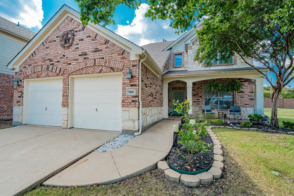 Traditional-style home featuring a front lawn, brick siding, covered porch, an attached garage, and driveway
