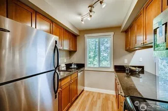 a kitchen with granite countertop a refrigerator a sink dishwasher a stove and a dining table with wooden floor