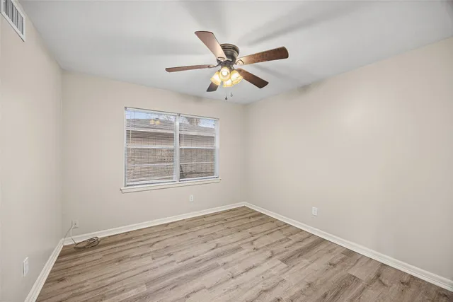 an empty room with wooden floor fan and windows