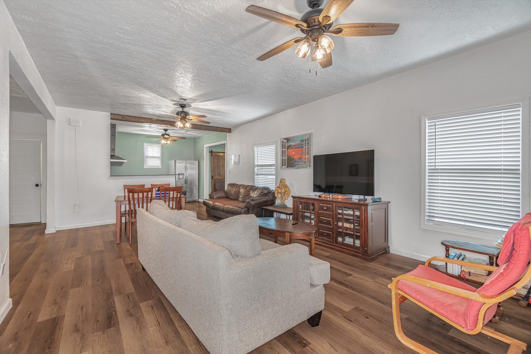 905 43rd Street Galveston, TX 77550 - Photo 29 of 43 This inviting open-concept living space features wood flooring, neutral walls, and ample natural light. It includes a cozy living area with ceiling fans, a dining area, and a modern kitchen with visible appliances. Perfect for comfortable living and entertaining.