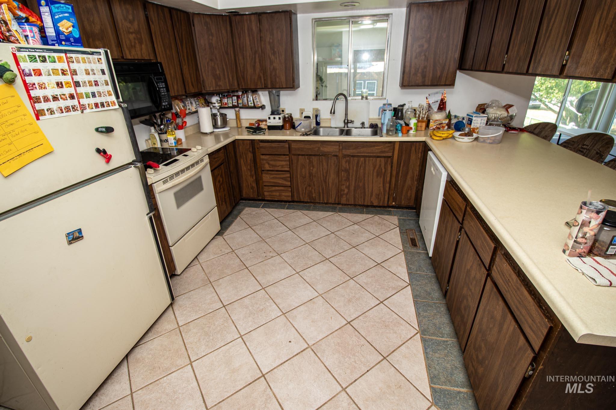 105 Weippe Avenue Weippe, ID 83553 - Photo 19 of 43 Kitchen with white appliances, light tile patterned flooring, light countertops, and dark brown cabinetry