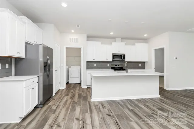 a view of kitchen with stainless steel appliances granite countertop a stove top oven a refrigerator and white cabinets with wooden floors