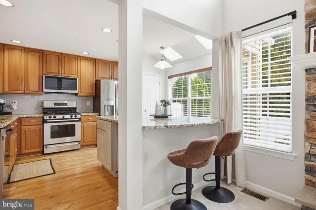 a kitchen with stainless steel appliances kitchen island granite countertop a stove a refrigerator and a dining table with wooden cabinet