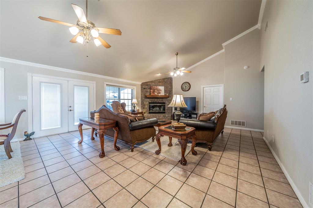 20175 Willow Glade Circle Pilot Point, TX 76258 - Photo 12 of 32 Living room with french doors, a brick fireplace, ceiling fan, crown molding, and light tile patterned floors