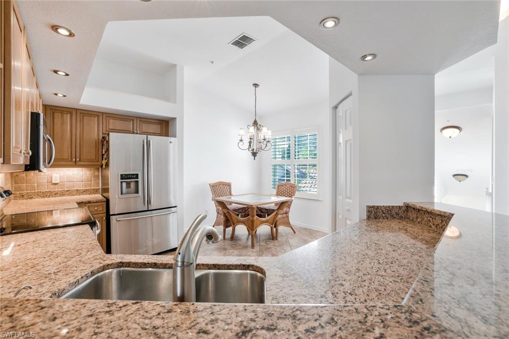 6914 Satinleaf Road North, Unit 202 Naples, FL 34109 - Photo 8 of 37 Kitchen featuring classic granite countertops, stainless steel appliances, backsplash with custom lighting and chandelier