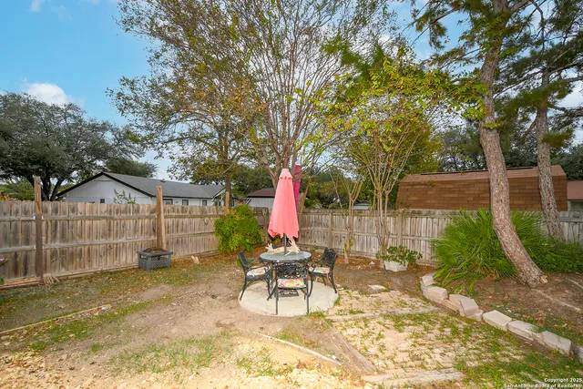 a view of a backyard with table and chairs potted plants and large tree
