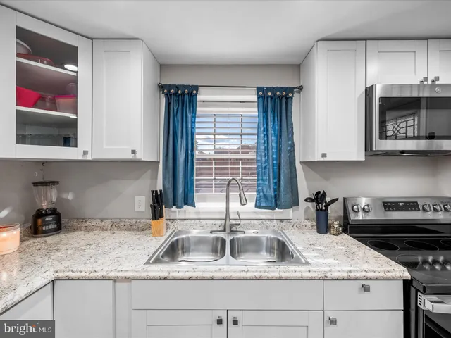 a kitchen with stainless steel appliances a stove top oven a sink a refrigerator white cabinets and wooden floor