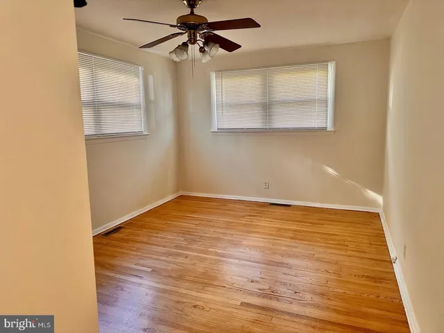an empty room with wooden floor fan and windows