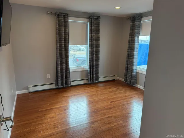 an empty room with wooden floor and windows with curtains