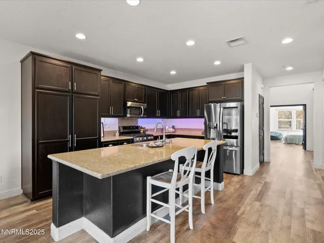 a kitchen with stainless steel appliances kitchen island granite countertop a refrigerator a stove a sink a dining table and chairs