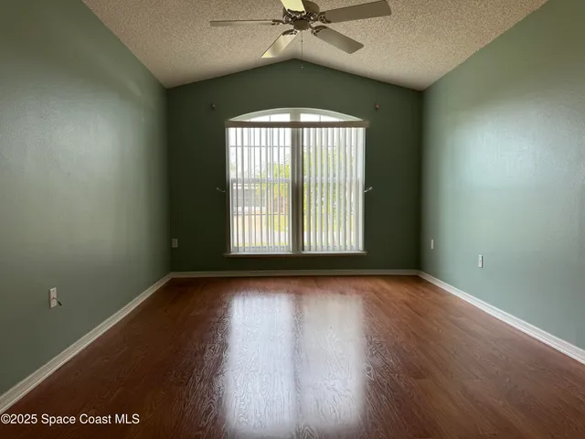 an empty room with wooden floor fan and windows
