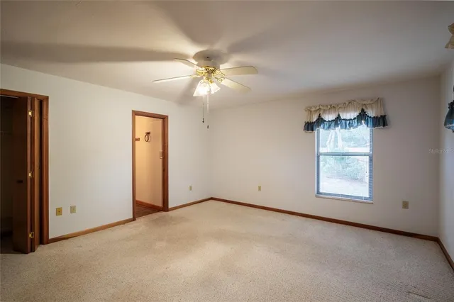 an empty room with chandelier fan and windows