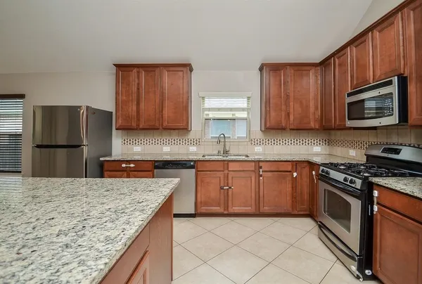 a kitchen with granite countertop wooden cabinets a stove top oven and stainless steel appliances