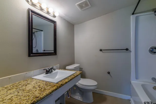 a bathroom with a granite countertop sink toilet and mirror