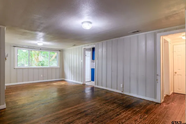 an empty room with wooden floor and windows with curtains