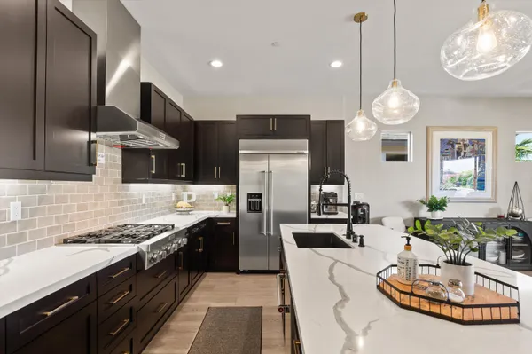 a kitchen with stainless steel appliances kitchen island granite countertop a stove a sink dishwasher a dining table and chairs with wooden floor